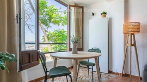 A room with a round table, two chairs, a potted plant, a standing lamp, and a view of trees through a window. - Cozy Studio in Heart of Nueva Andalucía - Pass the Keys (Marbella)
