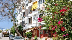 A residential street with parked cars, a tree with pink flowers, and a building with balconies and satellite dishes. - Cozy Studio in Heart of Nueva Andalucía - Pass the Keys (Marbella)
