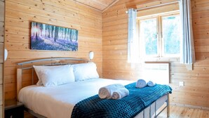 Une chambre dans une cabane en bois, avec un lit, un tableau et une fenêtre.