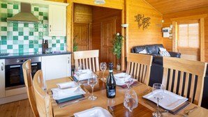 L’intérieur d’un chalet en bois comprend un coin repas aménagé pour un repas, une cuisine équipée d’appareils électroménagers modernes et un espace de vie chaleureux avec un canapé.