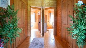 Un couloir en bois, orné d’un tapis, de deux plantes en pot et d’une porte donnant sur une autre pièce.