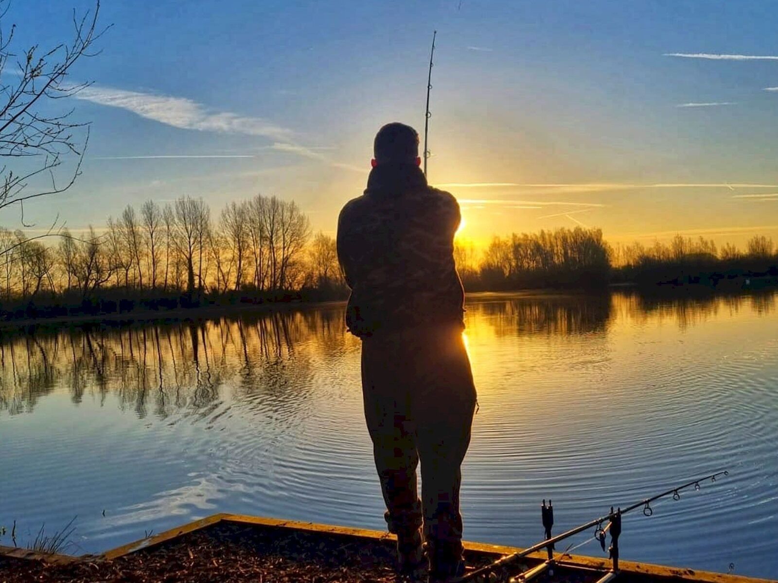 Eine Person beim Angeln an einem ruhigen See im Abendrot.