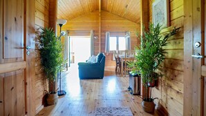 L’intérieur d’un chalet en bois, avec un plafond haut, un canapé, une table à manger et deux plantes en pot.