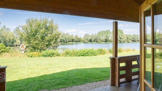 Un espace extérieur abrité, doté d’une terrasse en bois, d’un banc et offrant une vue sur un lac entouré d’arbres.