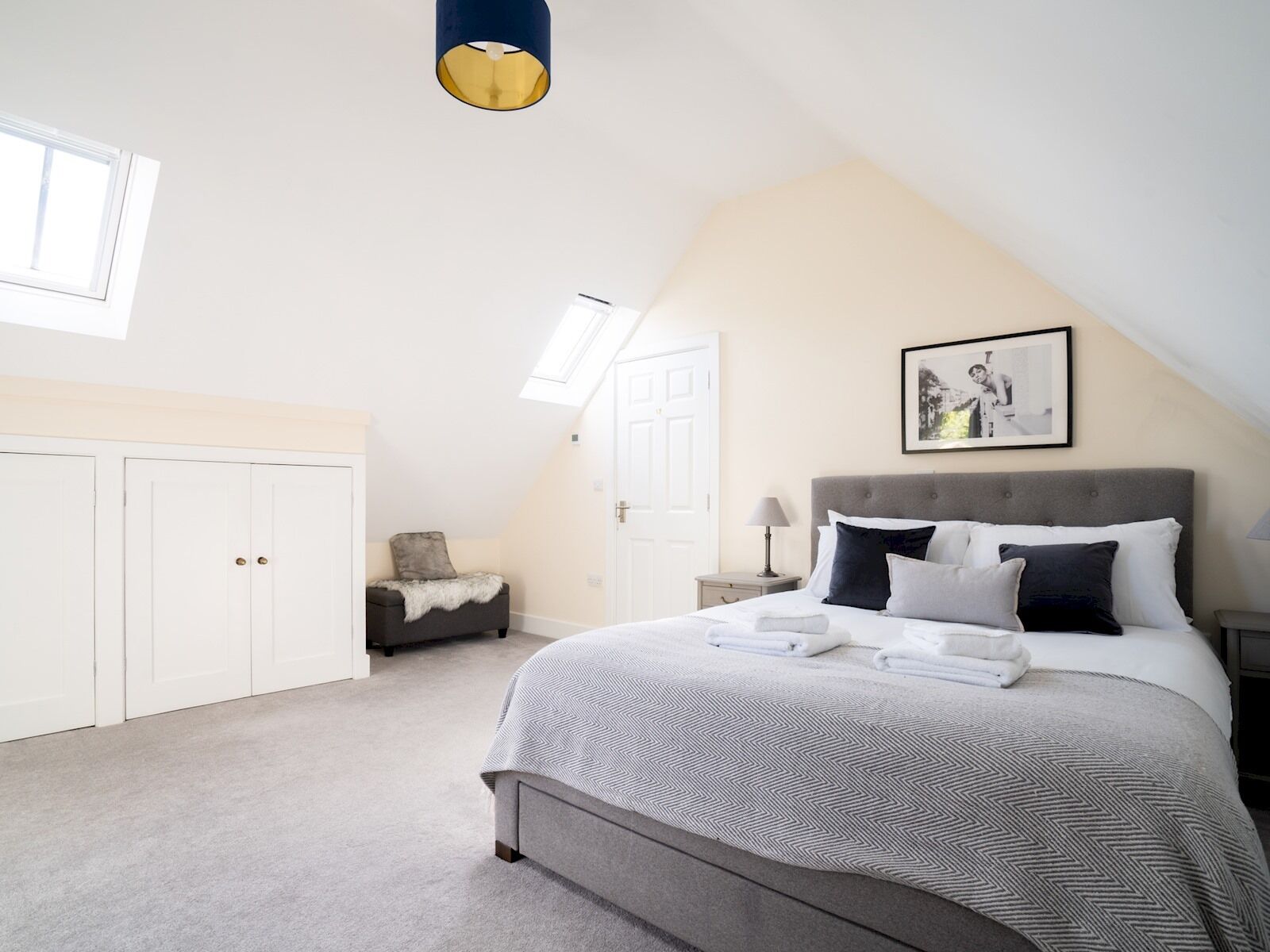 A bedroom with a large bed, a wardrobe, a nightstand, a lamp, and a framed picture on the wall.