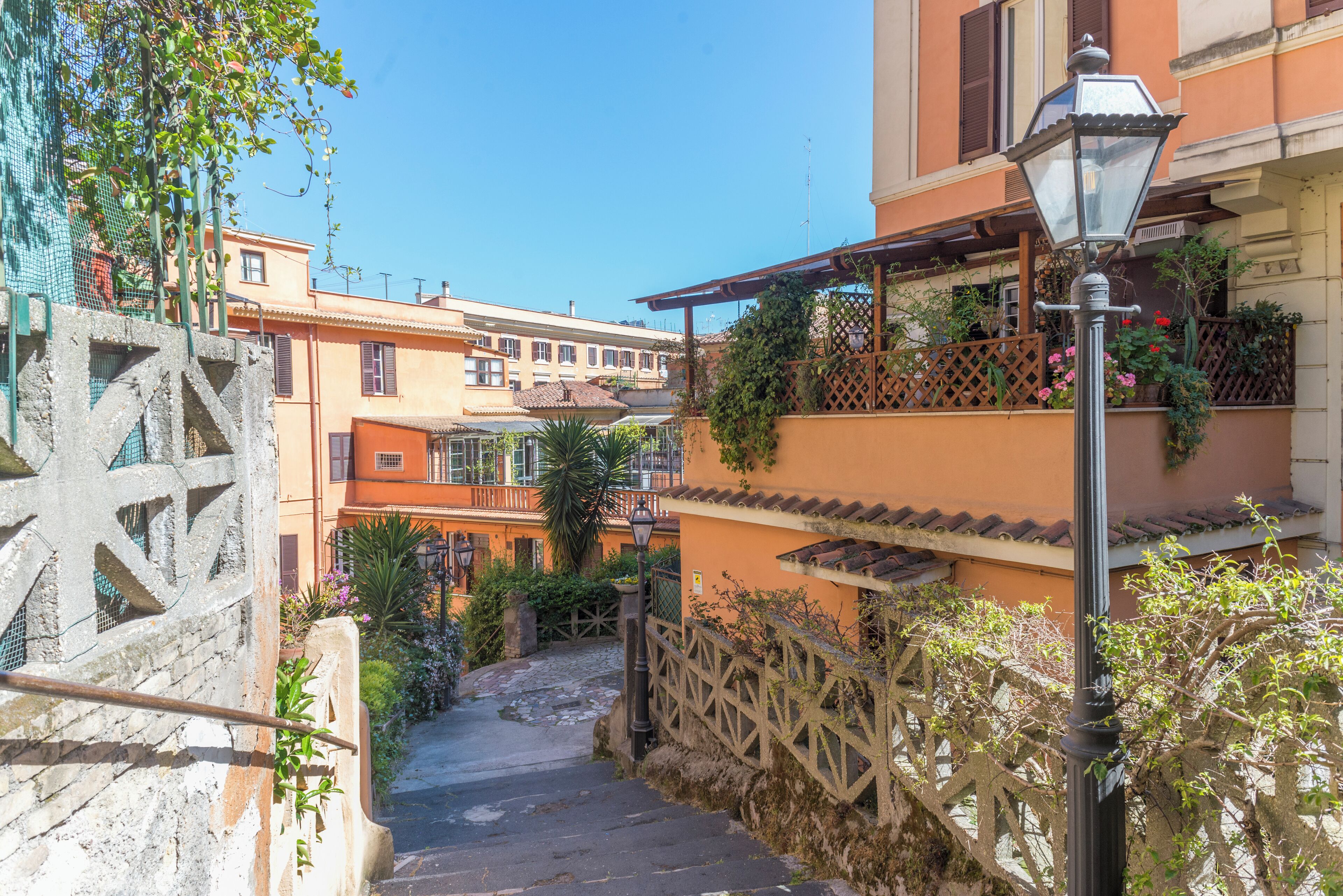 Una stretta scala in pietra conduce a un edificio con balconi, immerso nel verde sotto un cielo sereno.