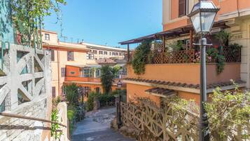 Una stretta scala in pietra conduce a un edificio con balconi, immerso nel verde sotto un cielo sereno.