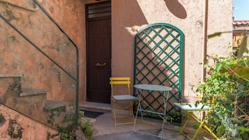 Un petit espace extérieur aménagé avec une table et des chaises en métal, une porte et une fenêtre à croisillons.