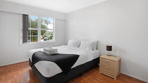 A modern bedroom with a bed, a bedside table, and a window. - Sunlit Glow Home with Parking and Air-con (Auckland Central Suburbs)