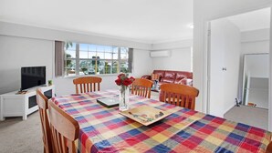 A modern living room with a dining table, chairs, a TV, and a window with a view of the outside. - Sunlit Glow Home with Parking and Air-con (Auckland Central Suburbs)
