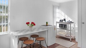 Una cocina compacta con encimera blanca, tres taburetes, un microondas y un refrigerador pequeño.