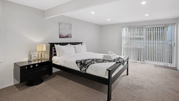 Un dormitorio moderno con cama, mesita de noche y ventana con persianas.