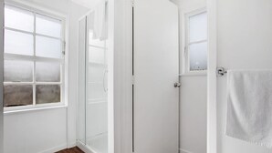 Un baño blanco con mampara de vidrio, ventana y una toalla colgada en la pared.