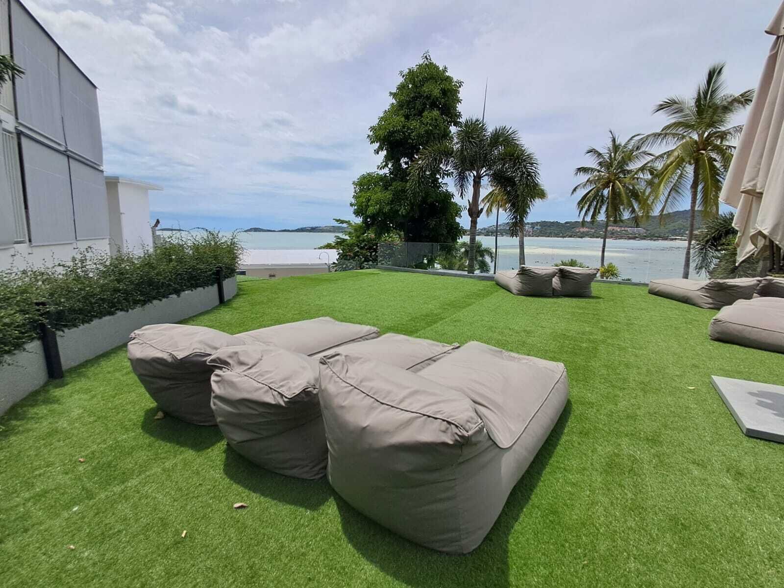 A patio with artificial grass, beige cushions, and a view of the sea.