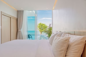 Habitación de hotel con una cama grande, vista al mar y un balcón con una silla.