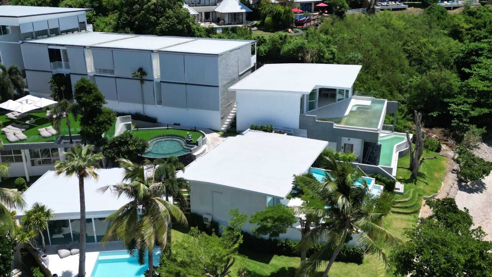 Un resort moderno con varias construcciones, piscina y abundante vegetación.
