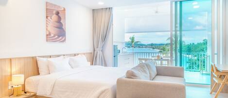 A hotel room with a bed, a sofa, a small table, a painting on the wall, and a balcony with a view.