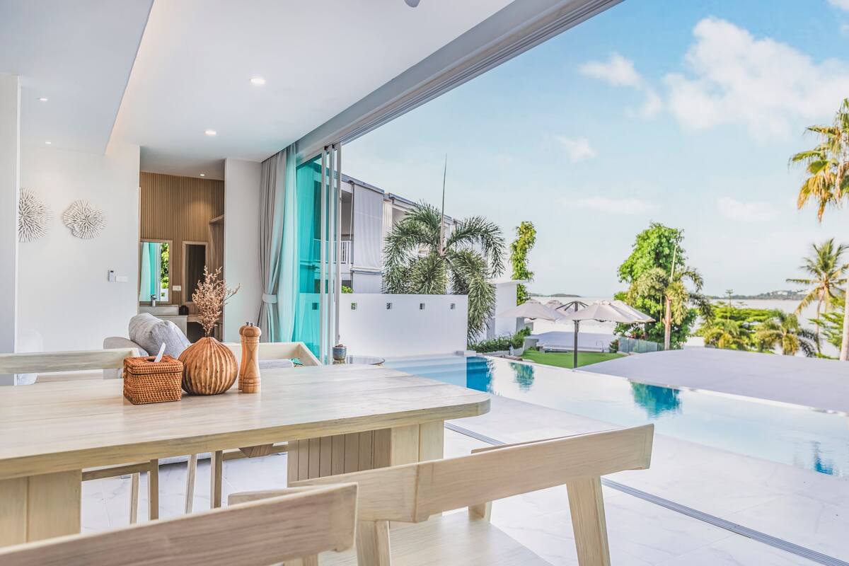A modern outdoor dining area with a pool and a view of a residential building.