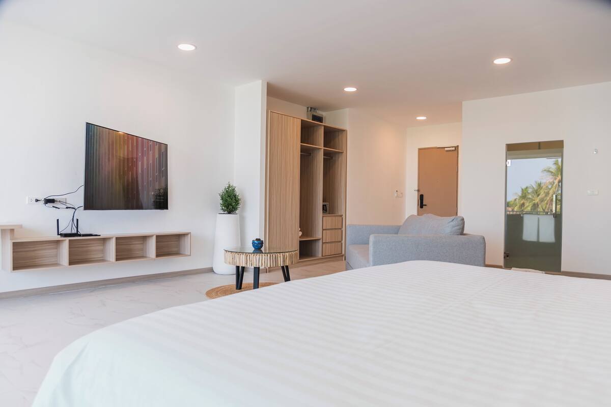 A modern bedroom with a large bed, a wardrobe, a seating area, and a TV mounted on the wall.