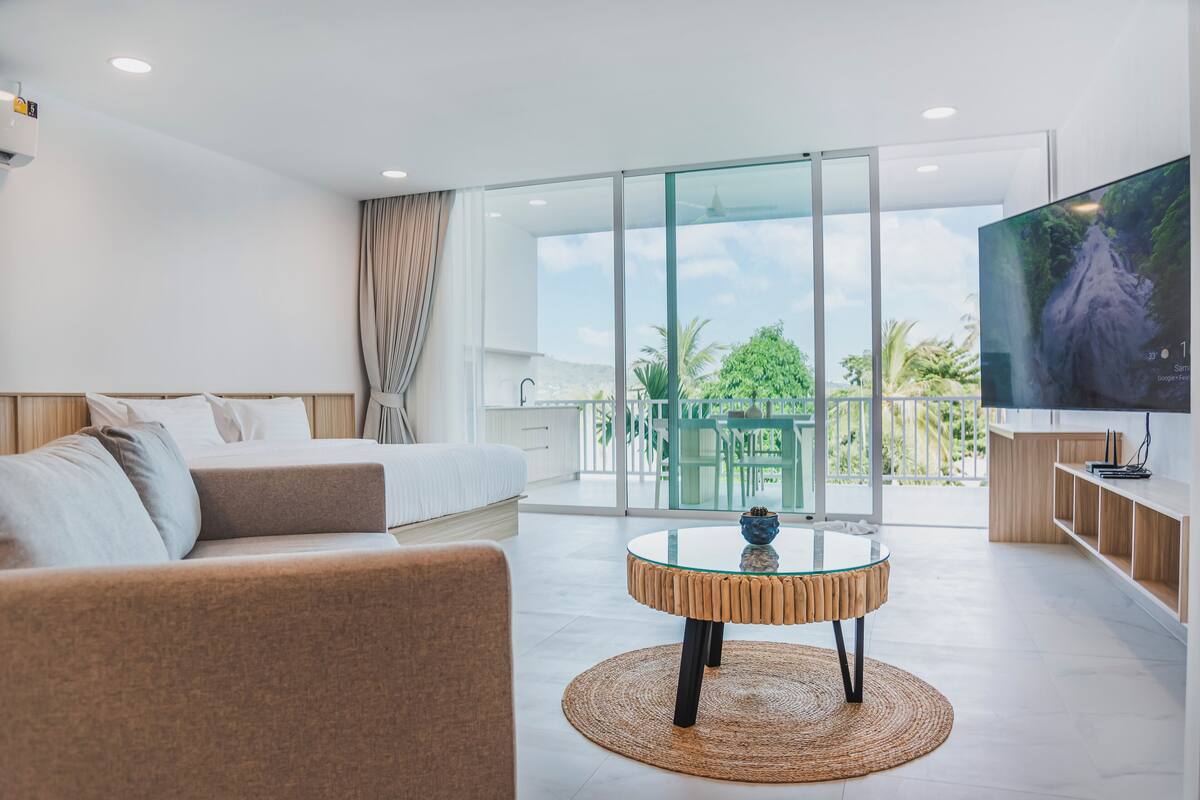 A modern hotel room with a bed, sofa, glass table, and a TV.