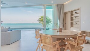 A modern dining area with a round table and wooden chairs, a sofa, and a view of the sea. - Replay Pool Villa  (Koh Samui)