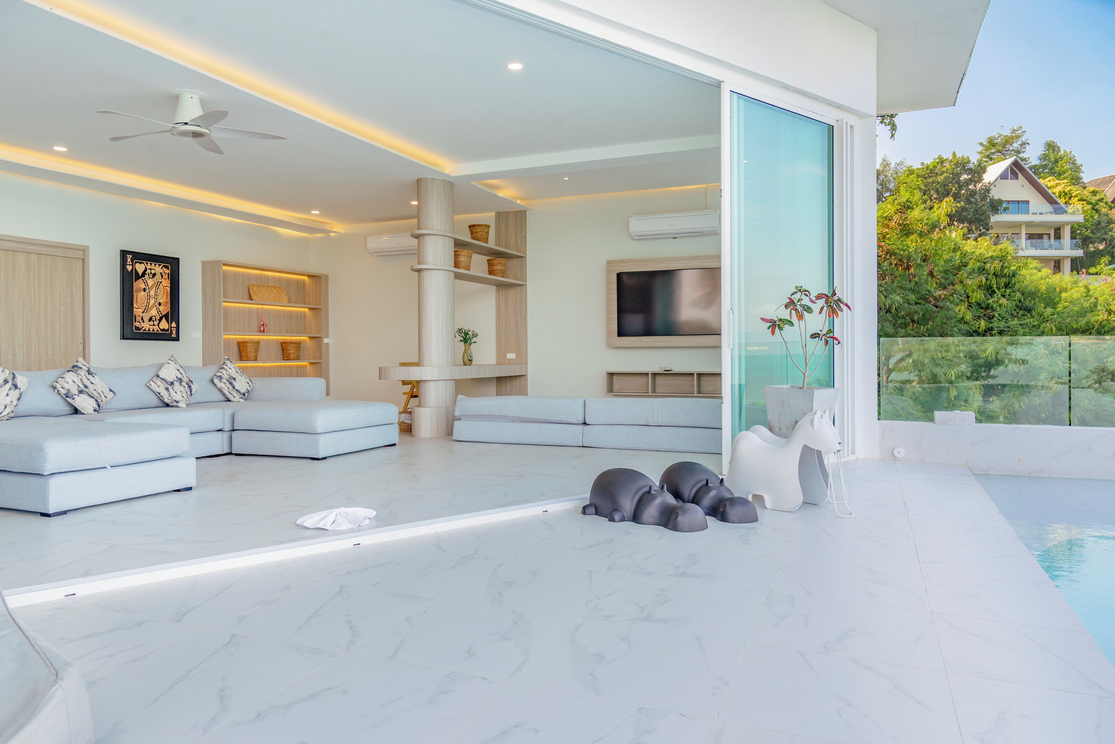 A modern living room with a sectional sofa, a flat-screen TV, and a glass door leading to a pool area.