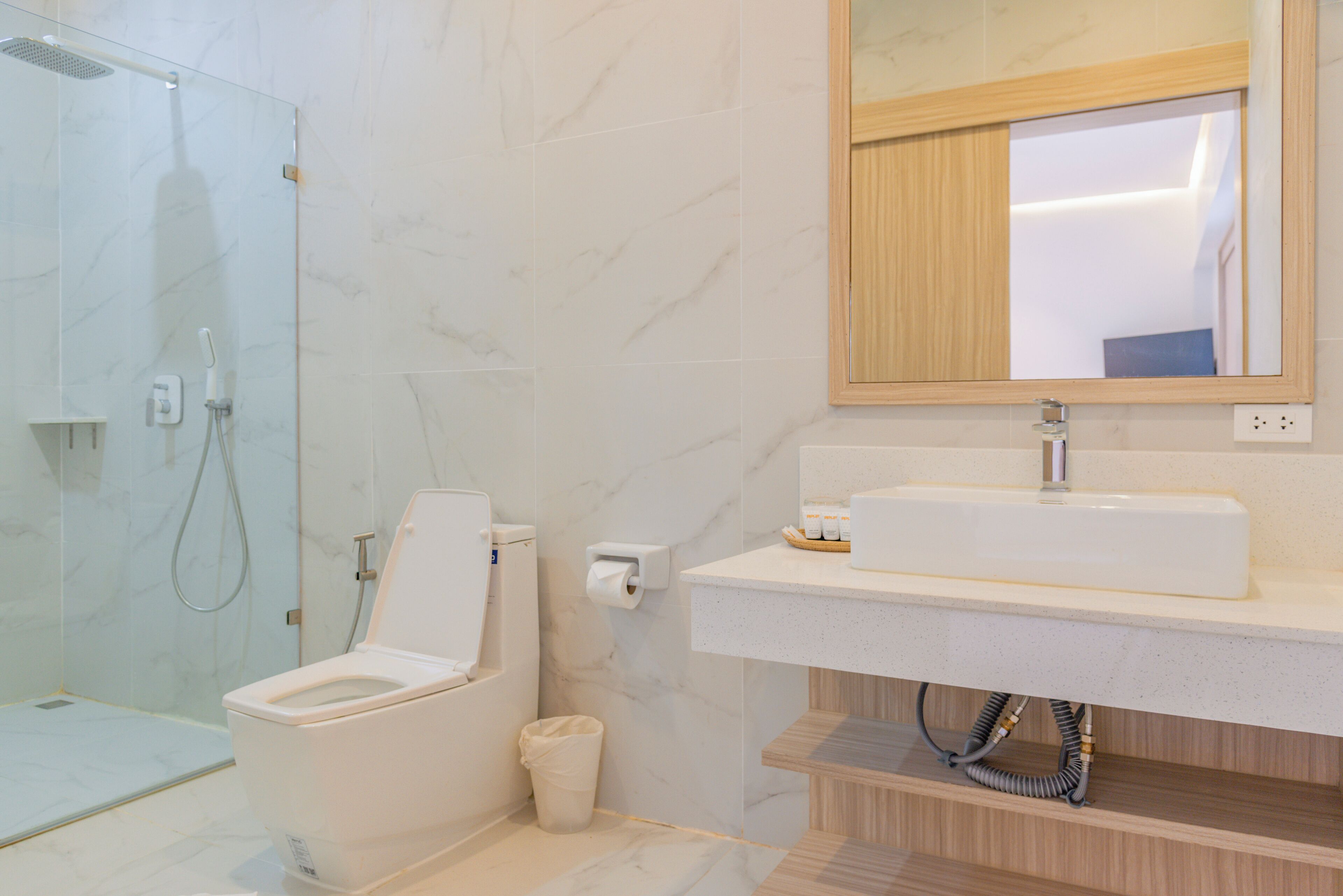 A modern bathroom with a glass shower enclosure, a toilet, a sink with a mirror above, and a toilet paper holder.