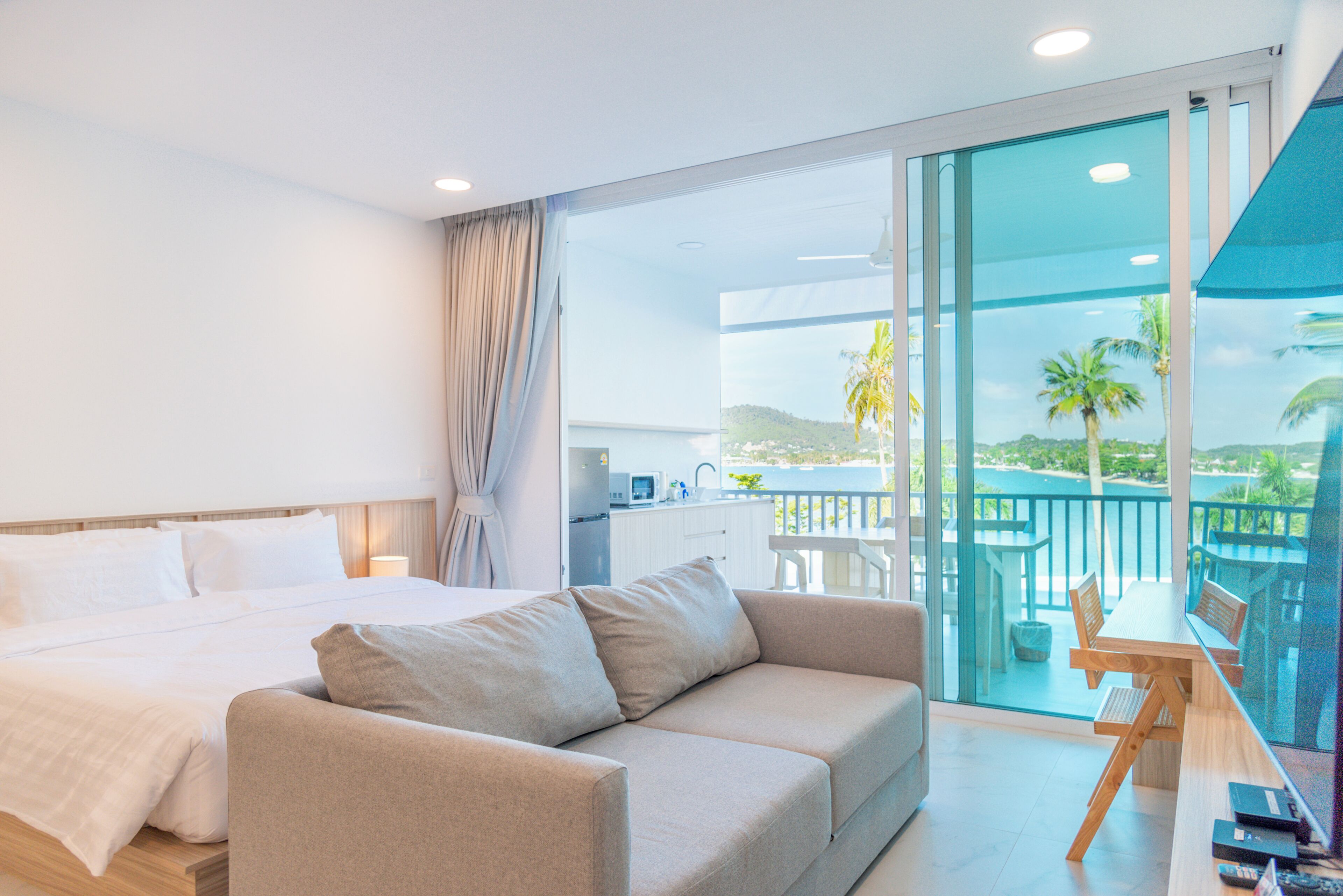 A hotel room with a bed, a sofa, a balcony with a view of the sea, and a dining area.