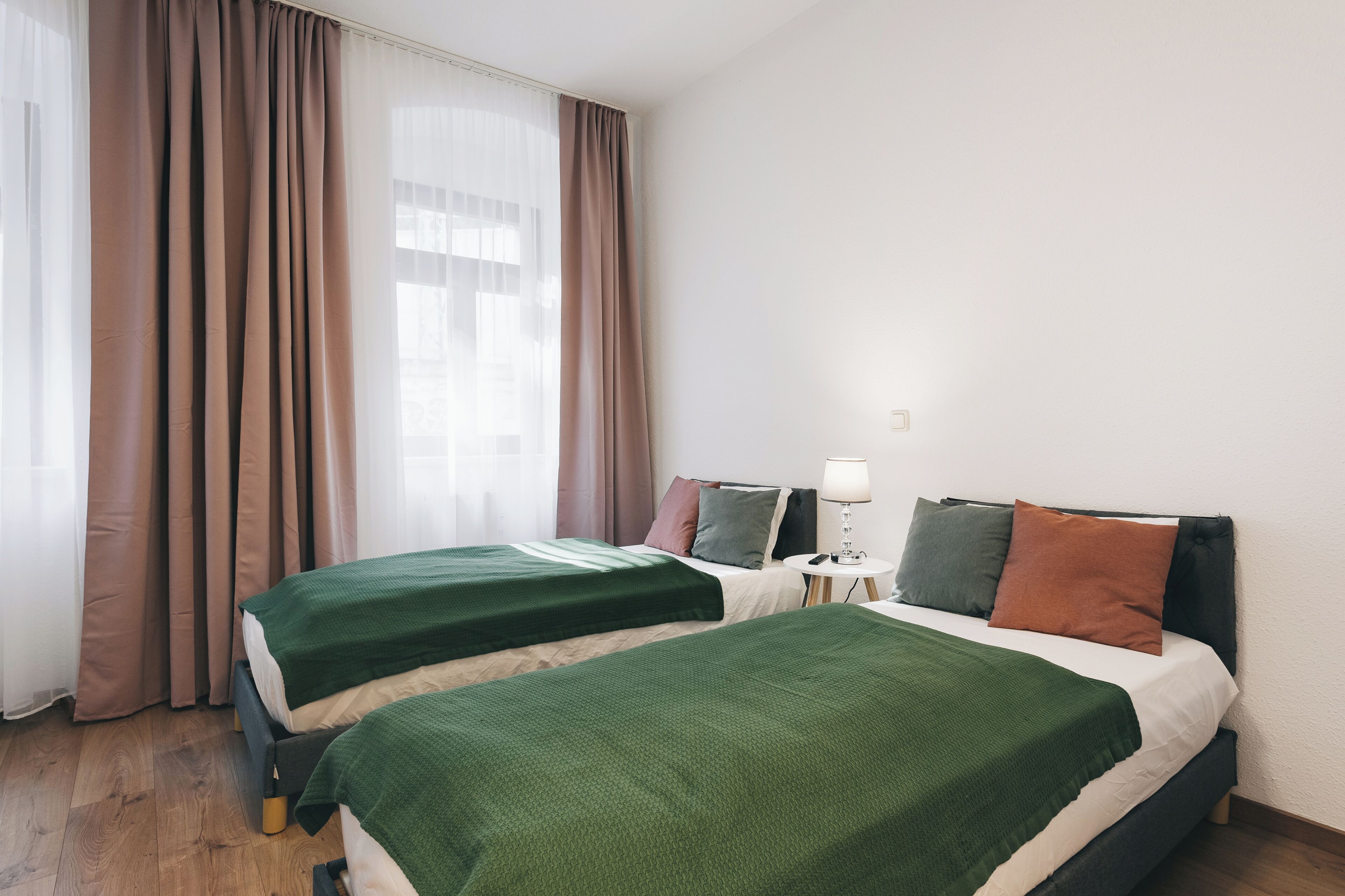 Une chambre d’hôtel avec deux lits, une table de chevet avec une lampe et une fenêtre avec des rideaux.