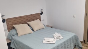 Un lit simple avec une tête de lit en bois, deux oreillers beige et une couvre-lit bleu clair. Deux serviettes blanches pliées sont posées sur le lit.