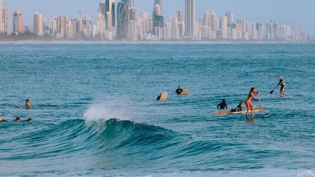 Paisagem costeira urbana com vista para o oceano, onde pessoas praticam atividades aquáticas.