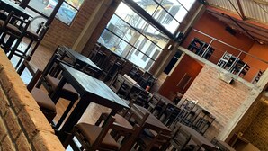 An indoor dining area with brick walls, large windows, and multiple tables and chairs. - Finca del Rincón (Guadalupe)