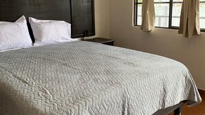 A neatly made bed with a quilted bedspread, a dark headboard, and a nightstand with a lamp. - Finca del Rincón (Guadalupe)