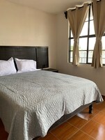 Una cama bien tendida con una colcha acolchada, un cabecero oscuro y una mesita de noche con una lámpara.