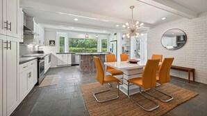 A modern kitchen with white cabinetry, a dining area with orange chairs, and a large island with a glass top. - "Whispering Oaks"  Enjoy this 4-bedroom home with HUGE backyard (Covington)