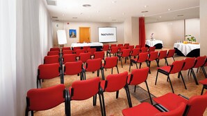 Ein Konferenzraum mit in Reihen angeordneten roten Stühlen, einer Whiteboard-Tafel und einer Projektionsleinwand, die 'hchhotels' zeigt.