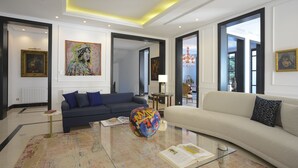 A modern living room with a dark blue sofa, a beige sofa, and a glass coffee table. There are two paintings on the walls and a chandelier in the corner. - L'Hôtel Particulier La Marsa (La Marsa)