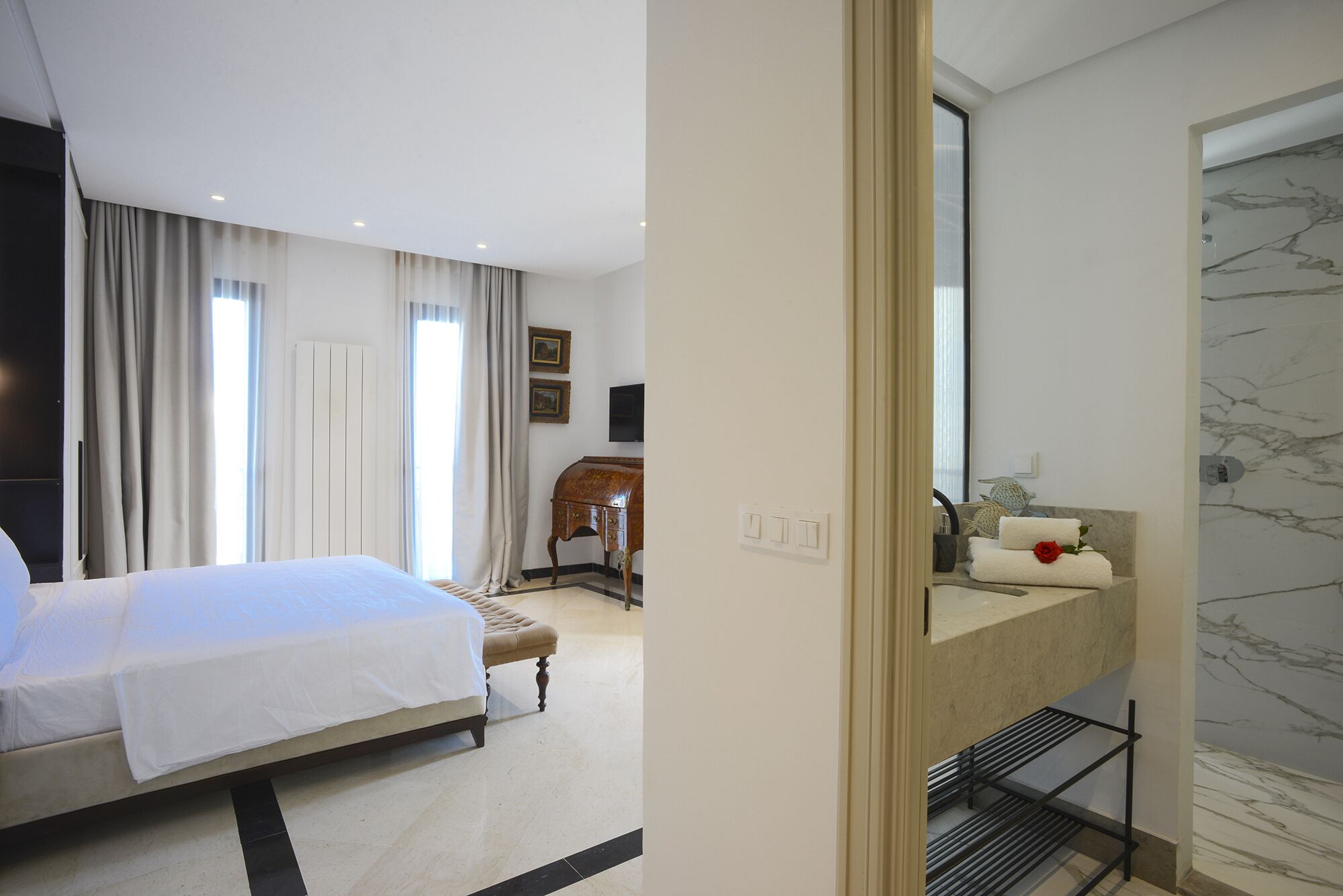 Habitación de hotel con cama, tocador de mármol, ducha y vistas al exterior.