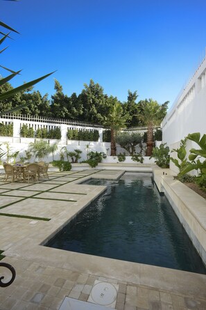 Piscina retangular com cerca branca e vegetação ao redor.