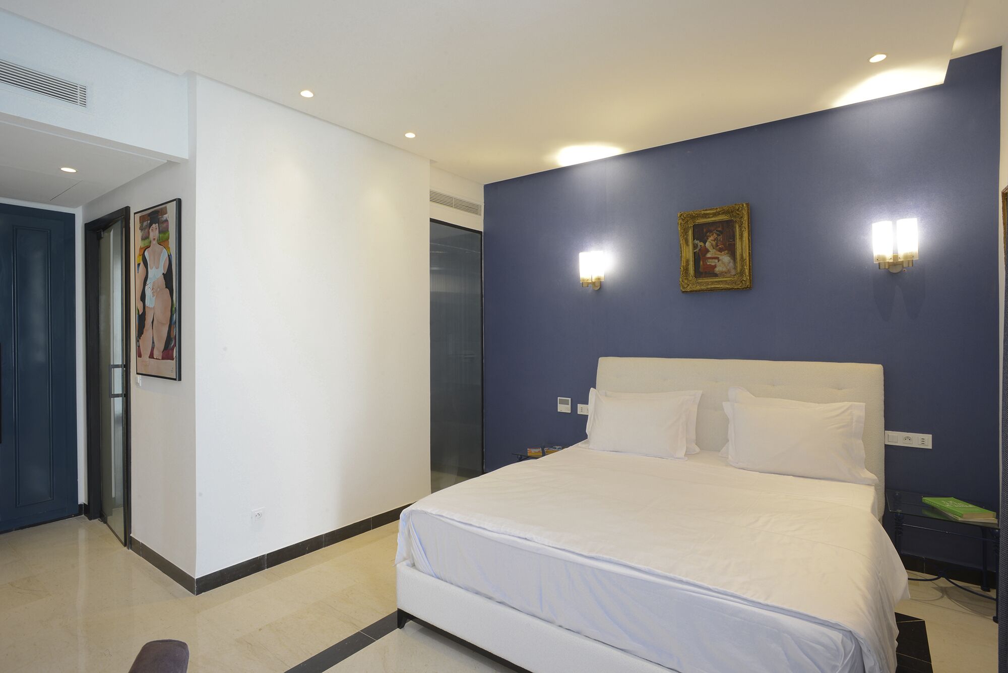 Une chambre d’hôtel avec un grand lit, du linge de lit blanc, un mur d’accent bleu et deux lampes fixées au mur.