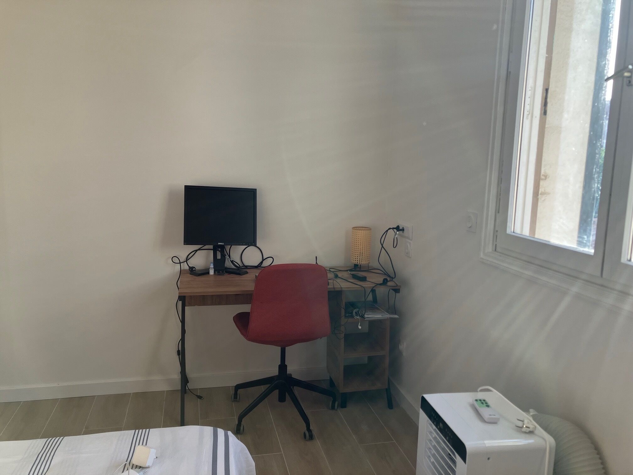 A small room with a desk, a computer, a red chair, a lamp, and a window.