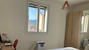 Ein Schlafzimmer mit einem Bett, einem Schreibtisch mit Computer, einem Fenster und einem Kleiderschrank.