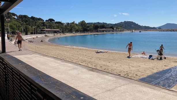 Ein Strand mit blauem Himmel, sandigem Ufer und einigen Personen.