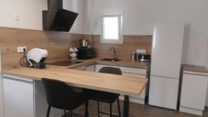 Eine moderne Küche mit Holzarbeitsplatte, Spüle, Herd und Kühlschrank. Zwei schwarze Stühle und ein Fenster über der Spüle.