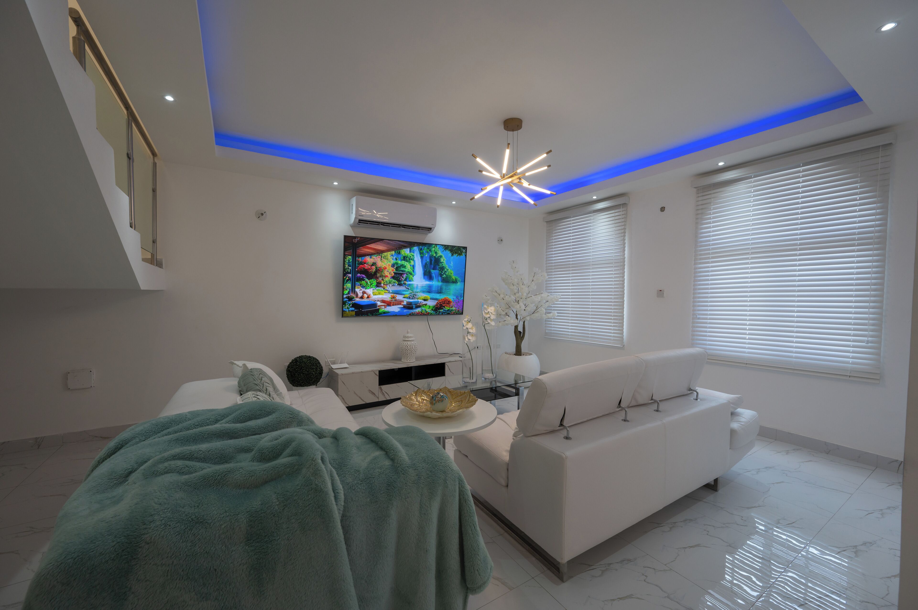 Una sala de estar moderna con un televisor de pantalla plana, un sofá blanco y una escalera.