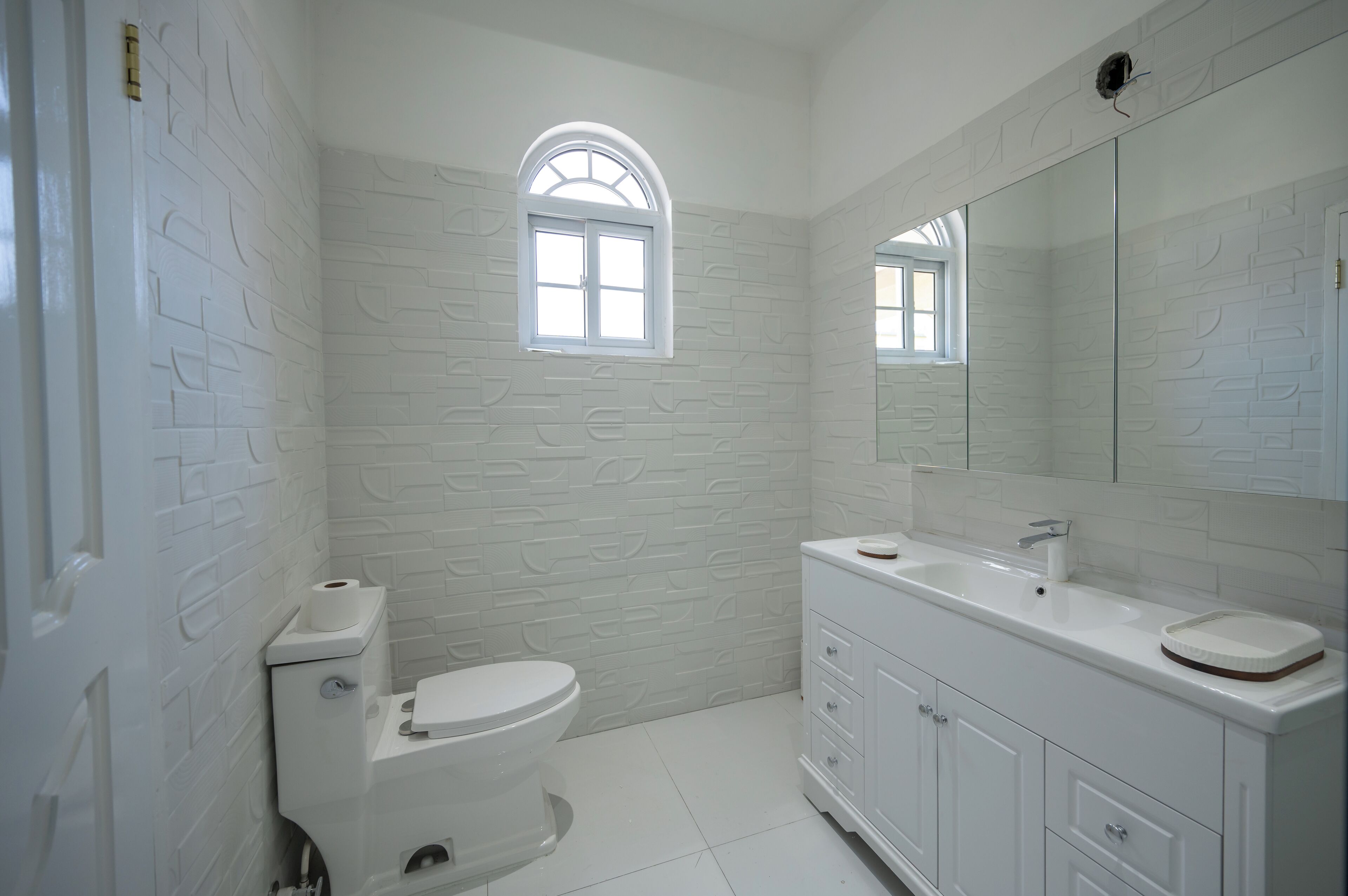 A bathroom with a white brick wall, a toilet, a sink with a mirror, and a window.