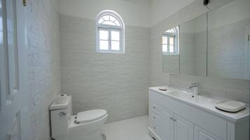 A bathroom with a white brick wall, a toilet, a sink with a mirror, and a window.