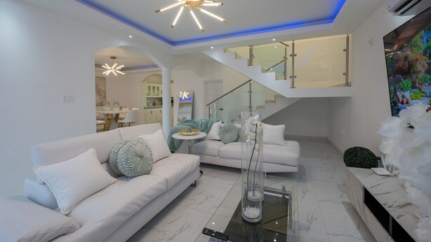 Una sala de estar moderna con un sofá blanco, una mesa de centro de vidrio y una escalera que sube a un nivel superior.