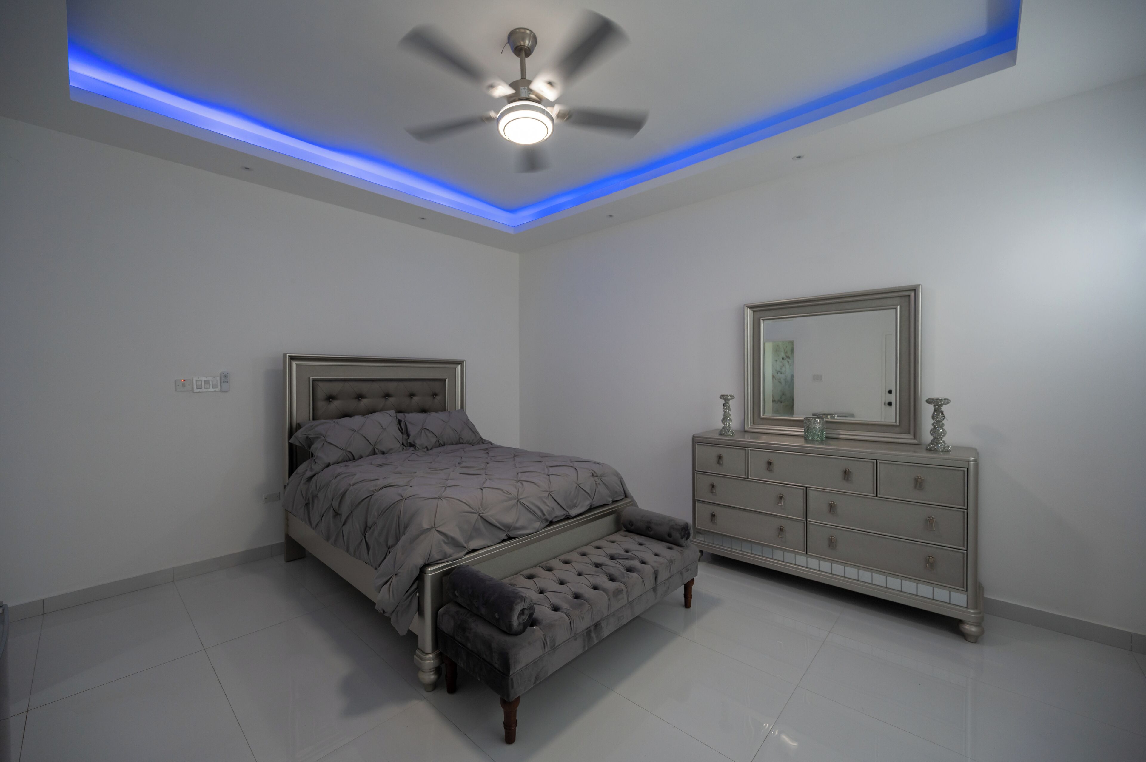 Une chambre à coucher avec un lit, un banc, une commode et un ventilateur de plafond.