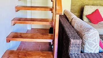 Un escalier en bois, doté d’une rampe, mène à un espace de vie comprenant un canapé et des coussins.